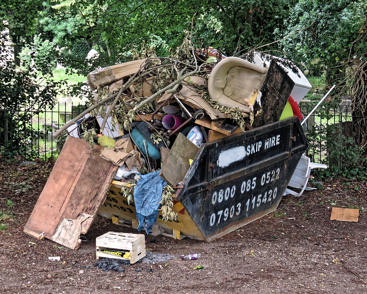A hire skip overflowing with furniture, garden waste and household junk on a London street