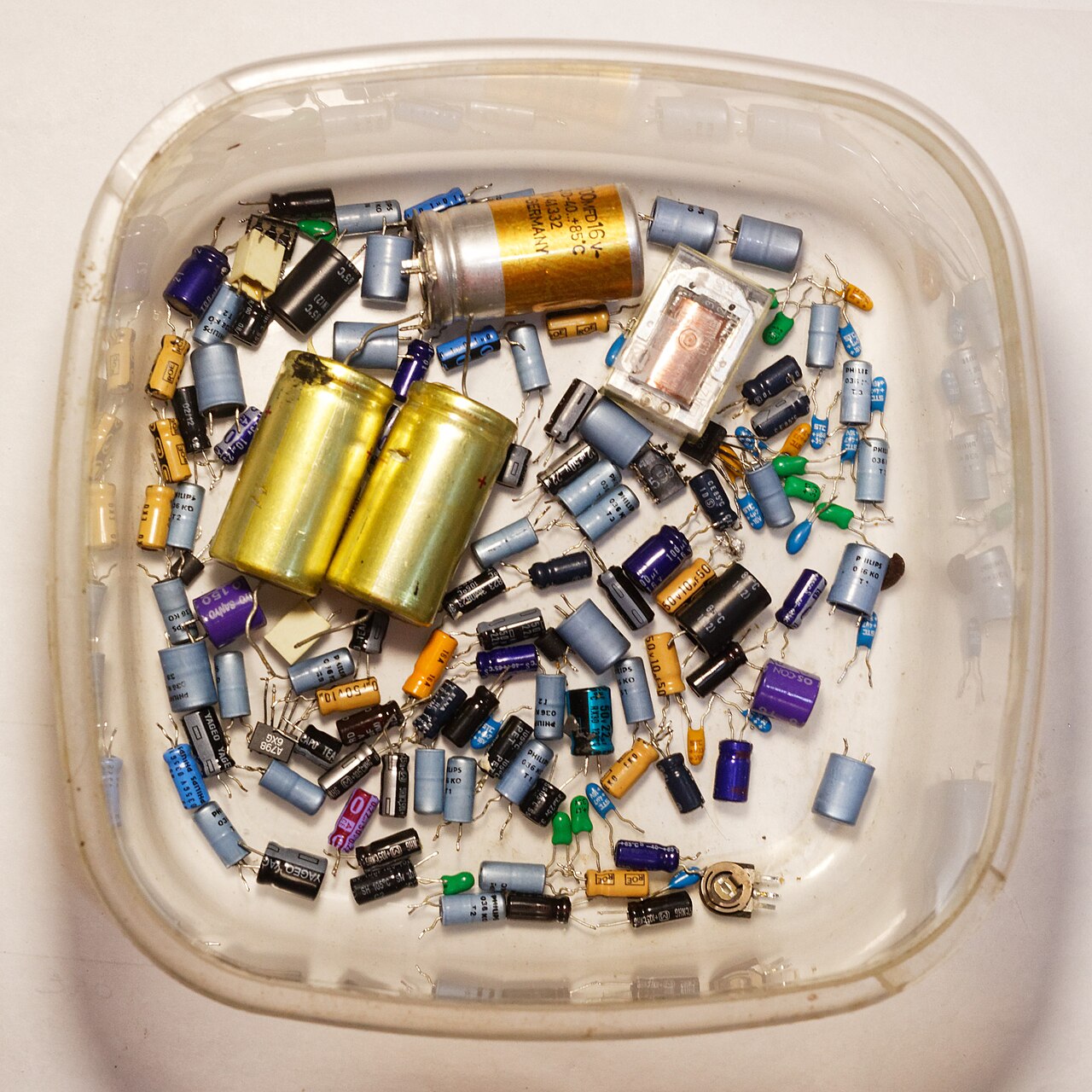 Dozens of salvaged capacitors from dismantled electronics collected in a plastic tub
