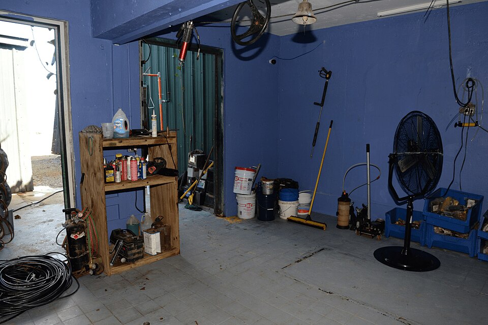 A cluttered garage with tools, buckets, paint and equipment lining the walls