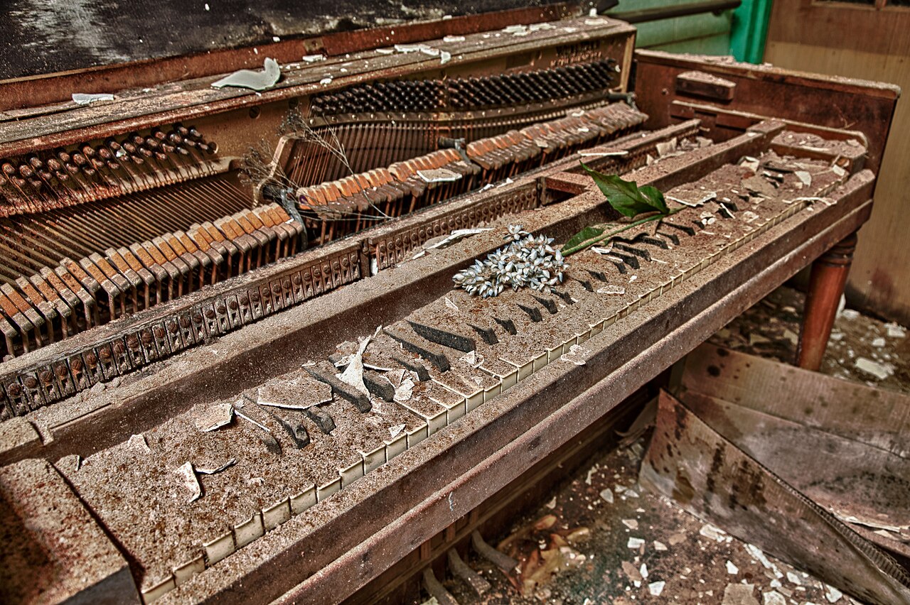The ruined keys and rusted strings of an abandoned upright piano, a flower resting on the keyboard